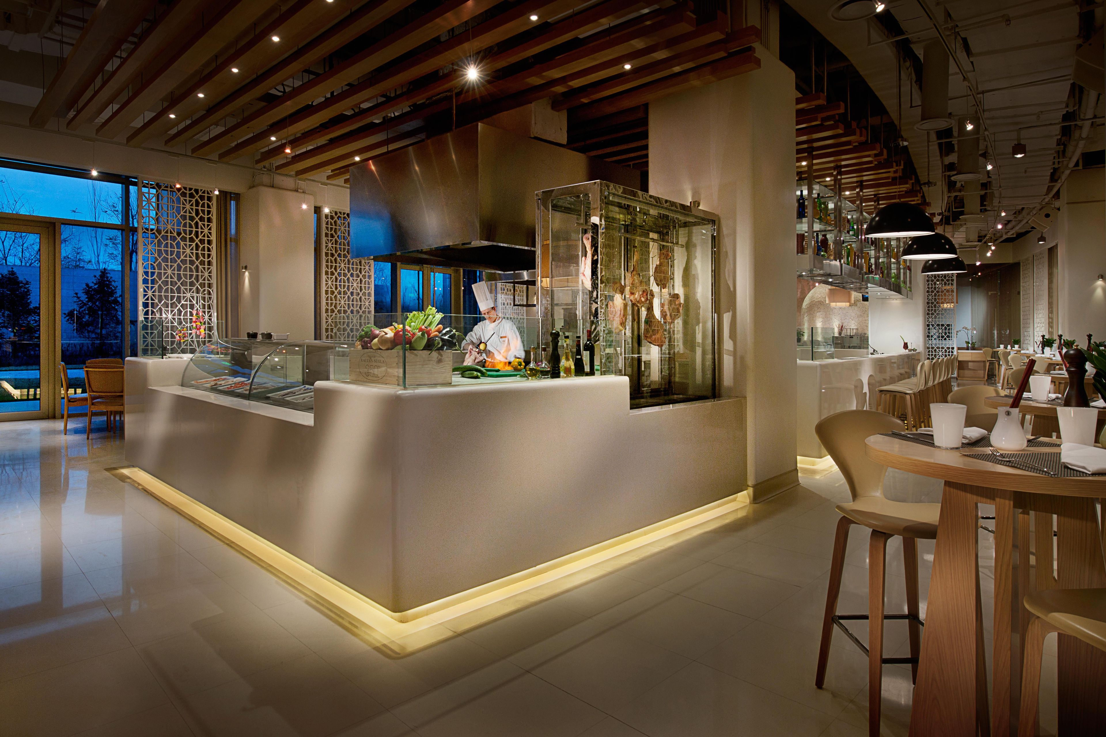 A modern restaurant interior with a central island, seating area, and a view of the outdoors.