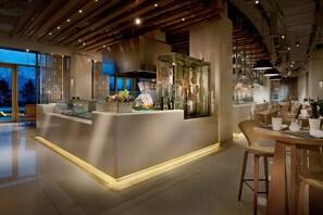 Ein modernes Restaurant-Interieur mit einer zentralen Kochinsel, einer Sitzgelegenheit und Blick ins Freie.