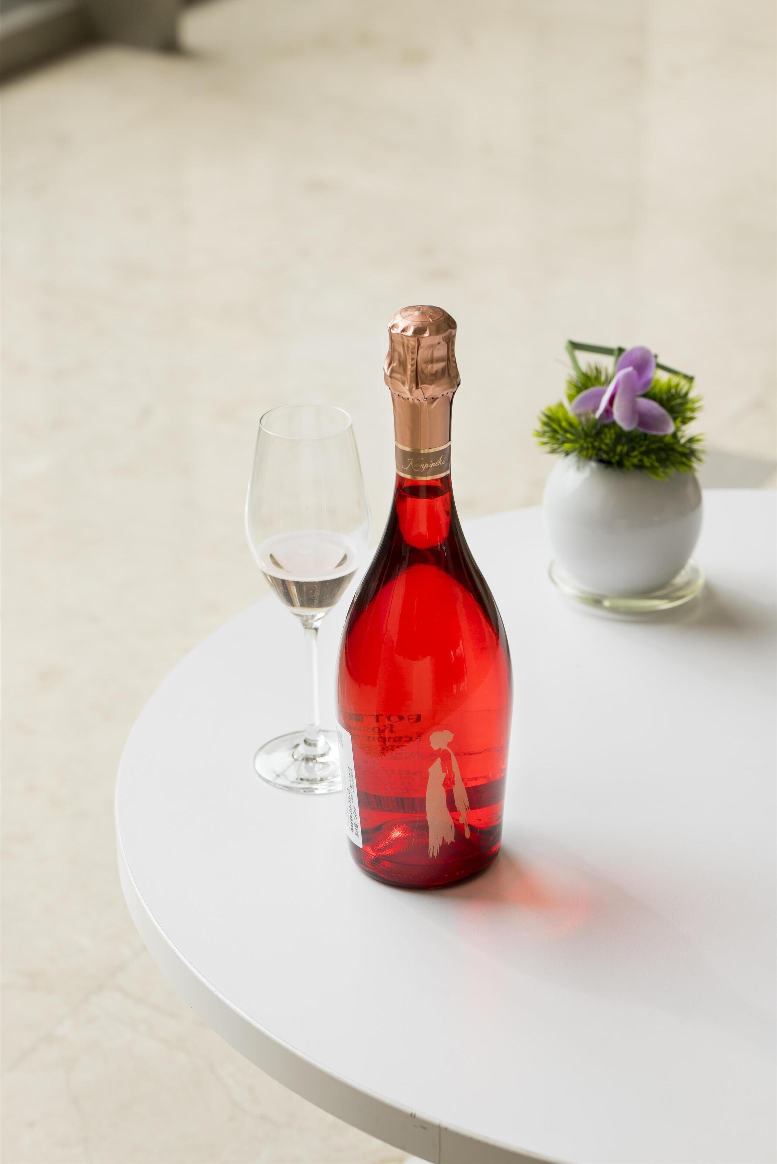 A red wine bottle and a wine glass on a white table.