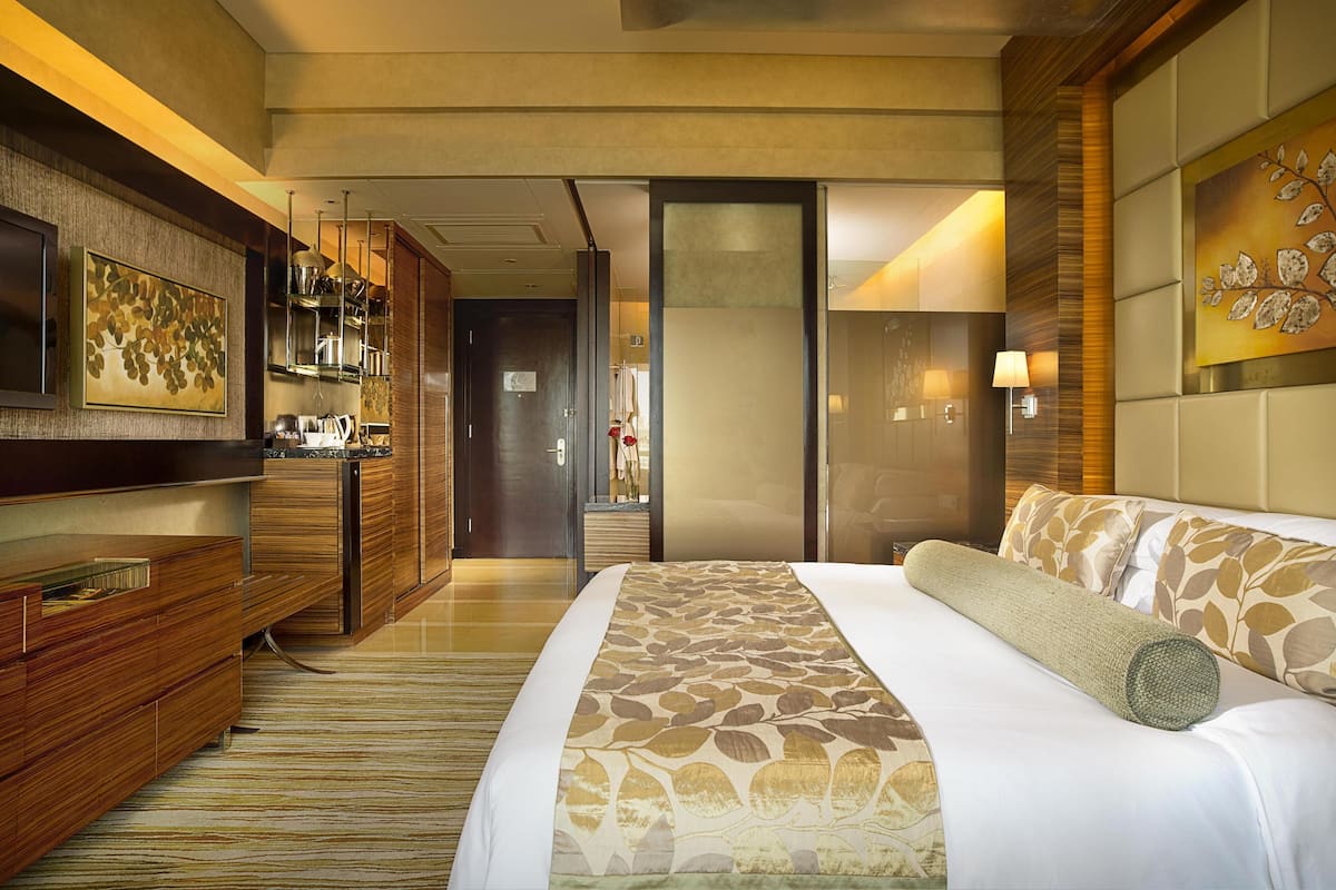 Habitación de hotel con una cama grande, televisión, cómoda de madera y baño visible a través de una puerta abierta.