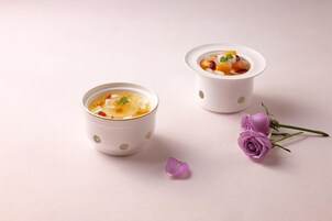 Dos tazas blancas con lunares que contienen un postre y una rosa morada con pétalos sobre una superficie lisa.