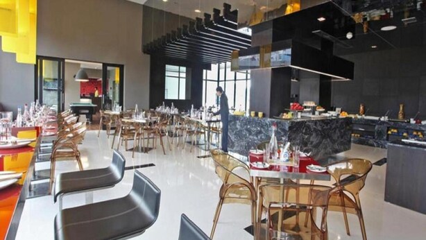 Um restaurante moderno com um amplo espaço para refeições, diversas mesas e um bar com bancadas de mármore.