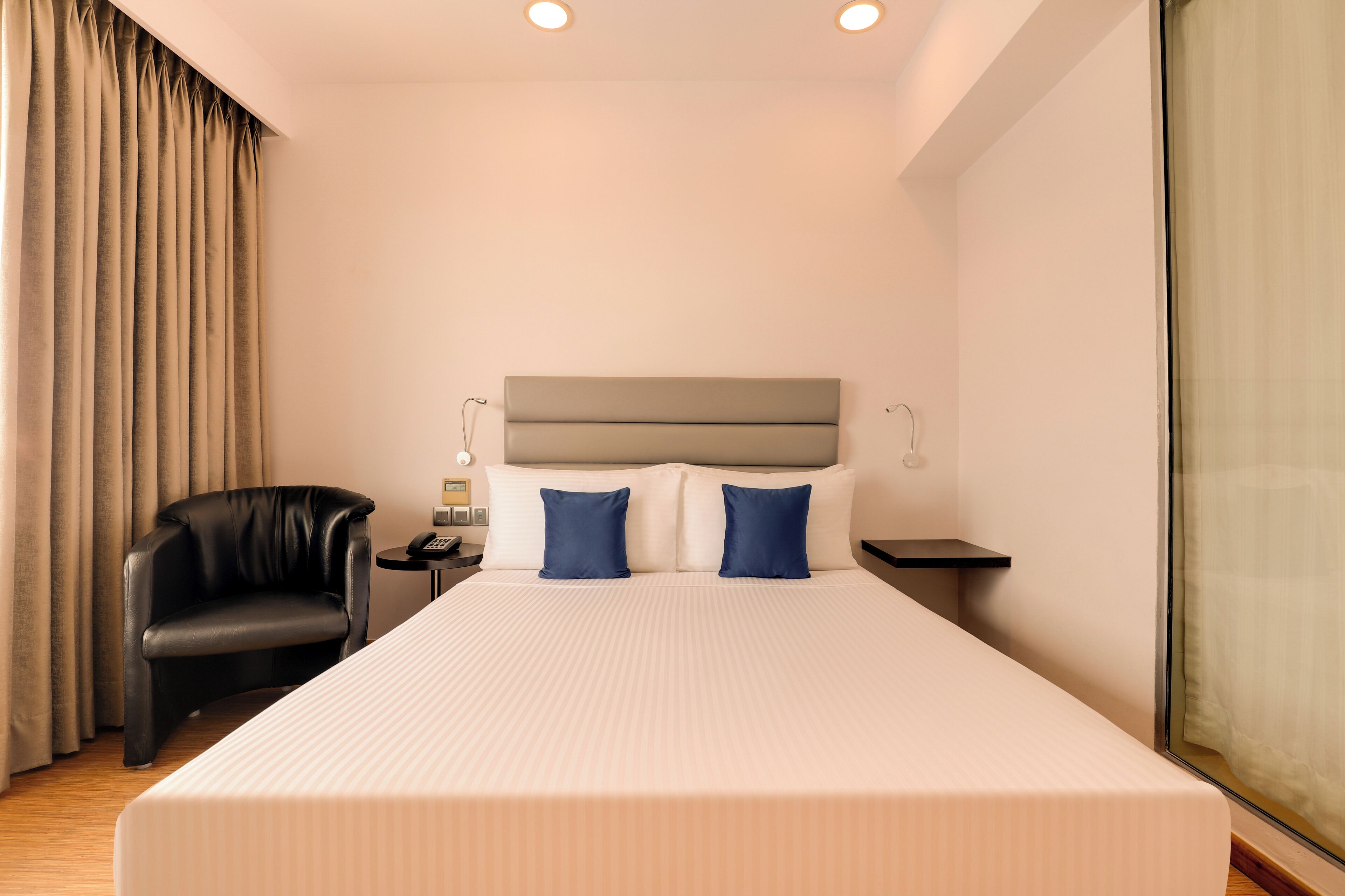 A hotel room with a large bed, a headboard, a desk with a lamp, a chair, and a window with curtains.
