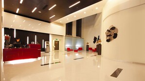 Um hall amplo com um balcão de recepção vermelho, iluminação moderna e piso limpo e bem cuidado.