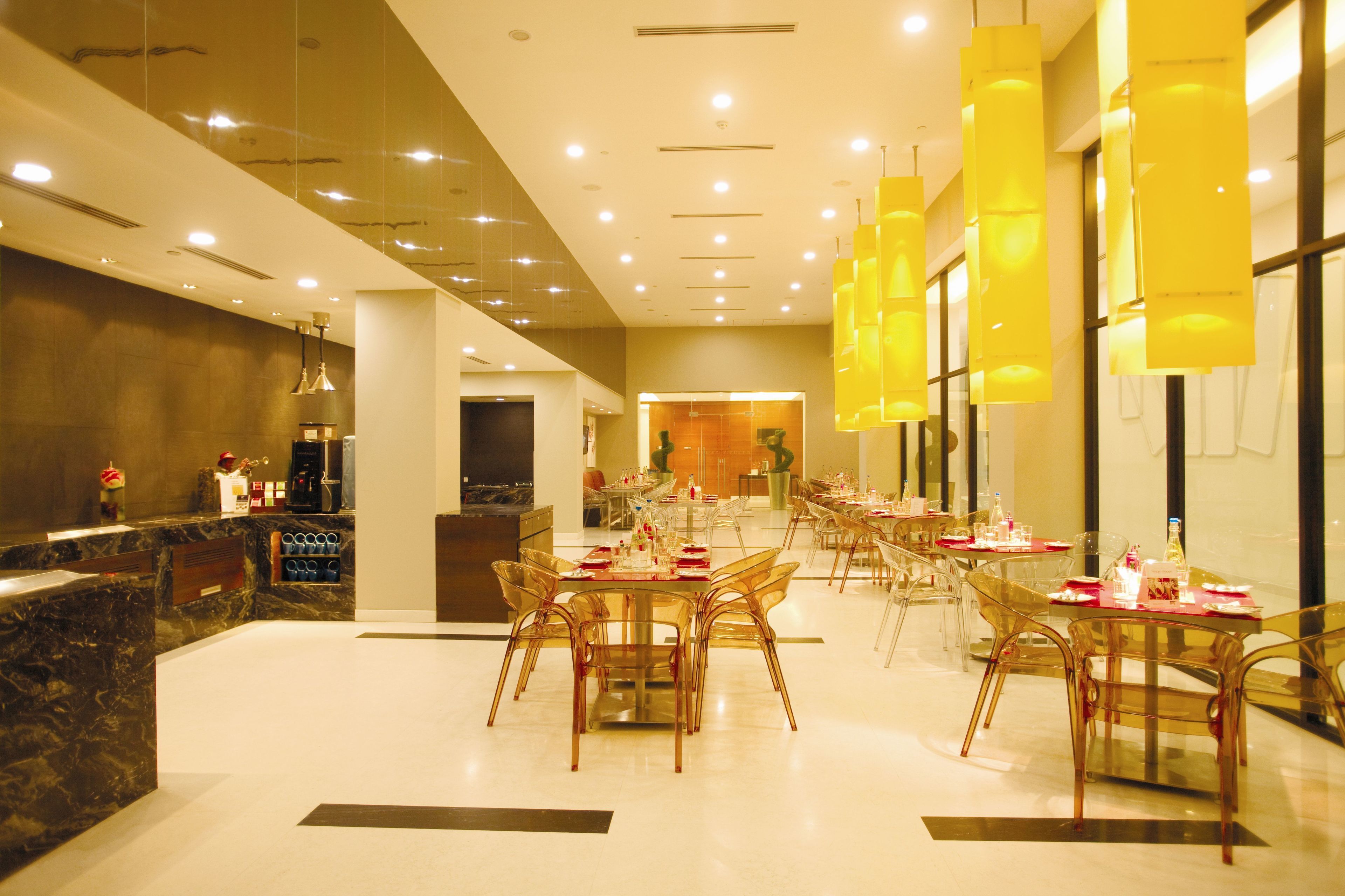 A modern hotel lobby with a marble reception desk, clear glass chairs, and yellow pendant lighting.