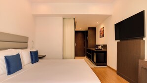 Quarto de hotel com uma cama grande, TV fixada na parede e uma pequena área de cozinha.