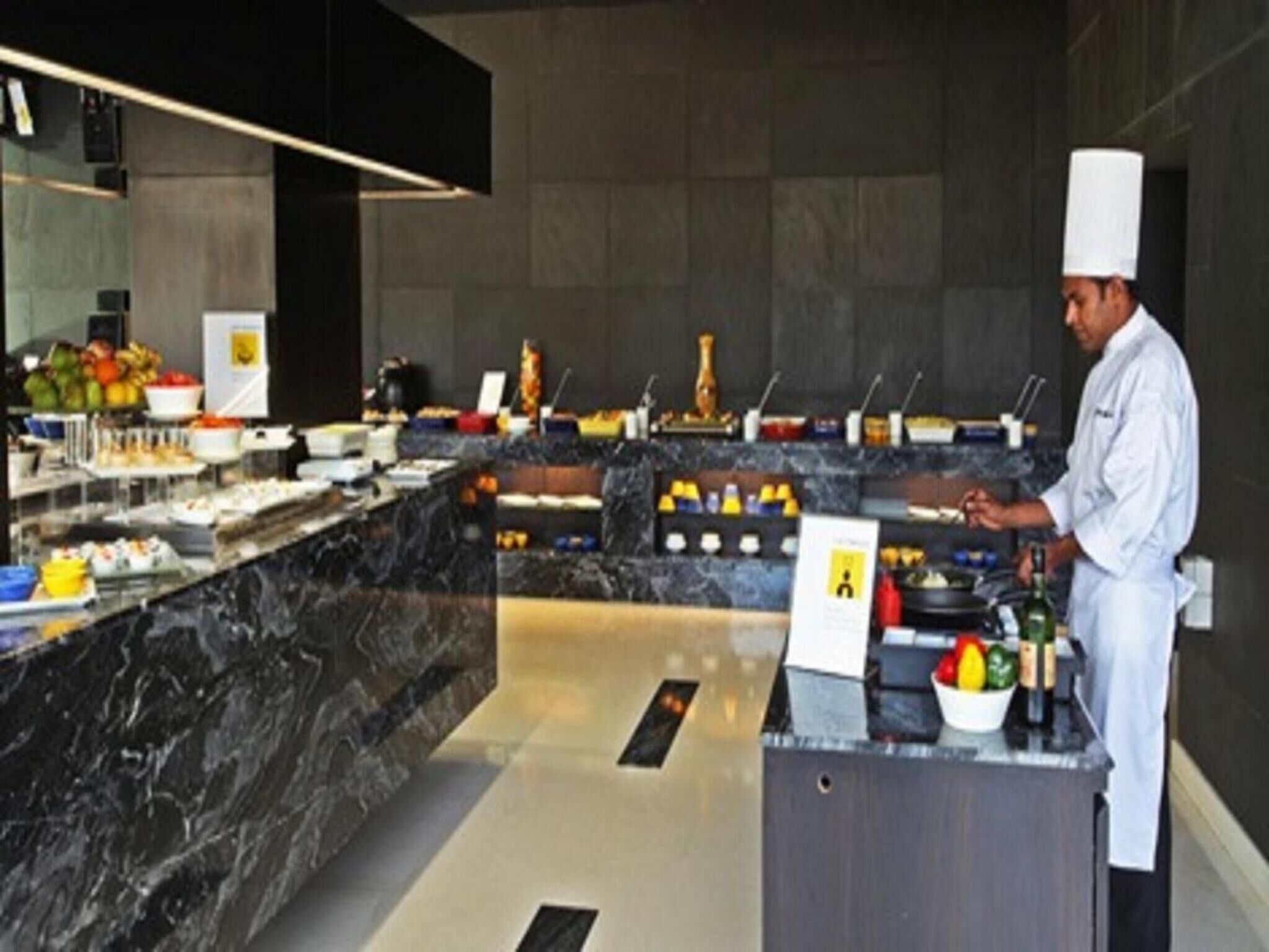 Um chef prepara alimentos em uma cozinha moderna com bancadas de mármore e diversos utensílios e ingredientes culinários.