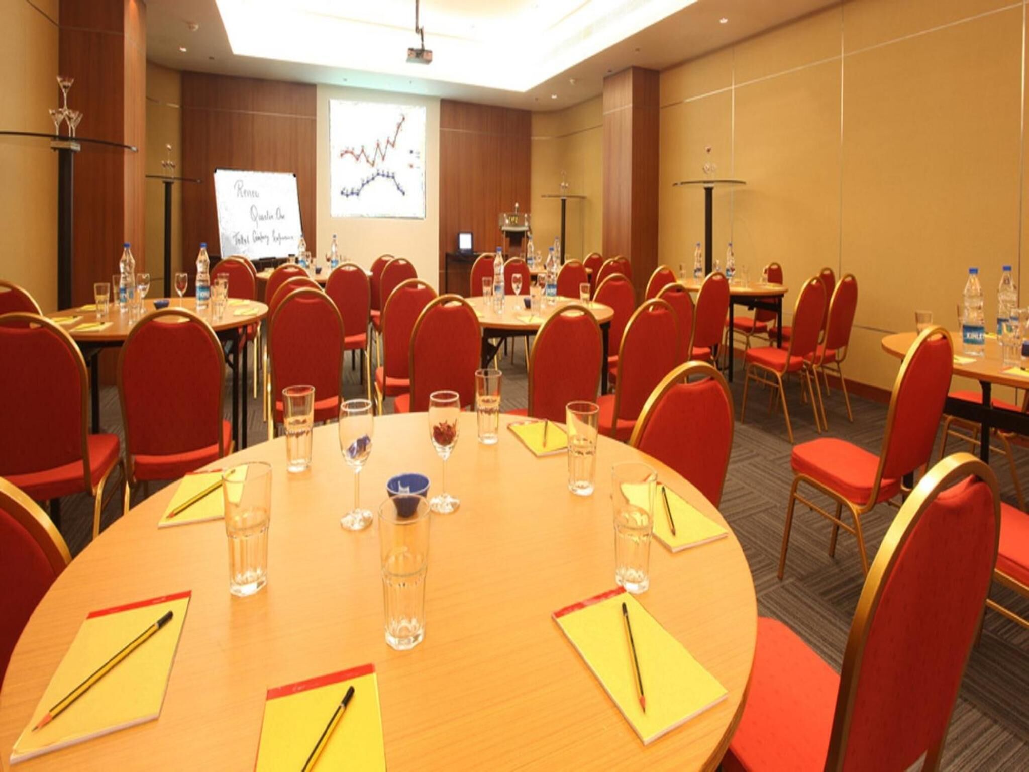 A conference room with round tables, red chairs, and a presentation screen.