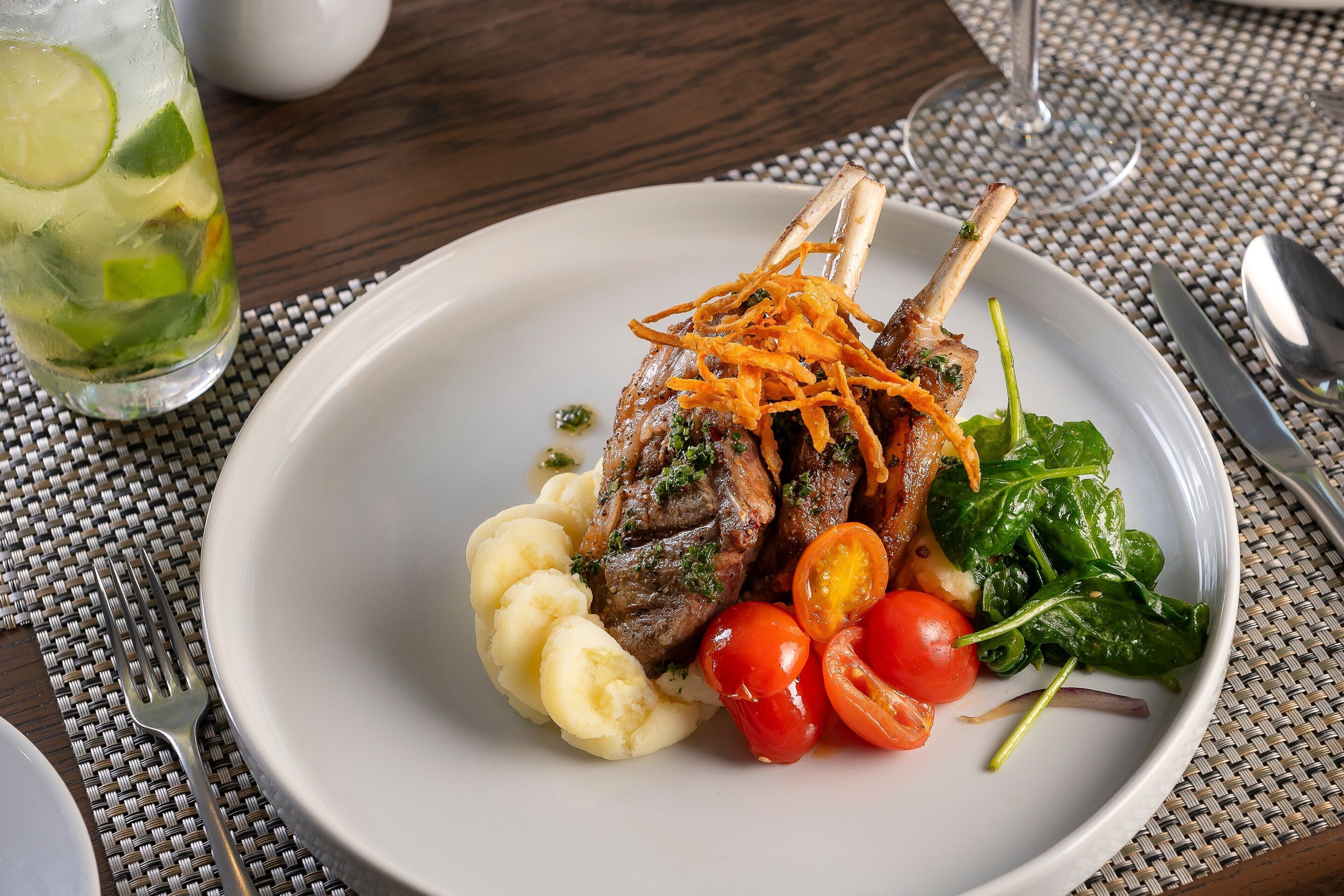 Une assiette de nourriture comprenant des côtelettes d’agneau, de la purée de pommes de terre, des tomates cerises et des épinards.
