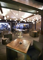 Un interior de restaurante moderno con mesas redondas, sillas de mimbre e iluminación esférica colgante.