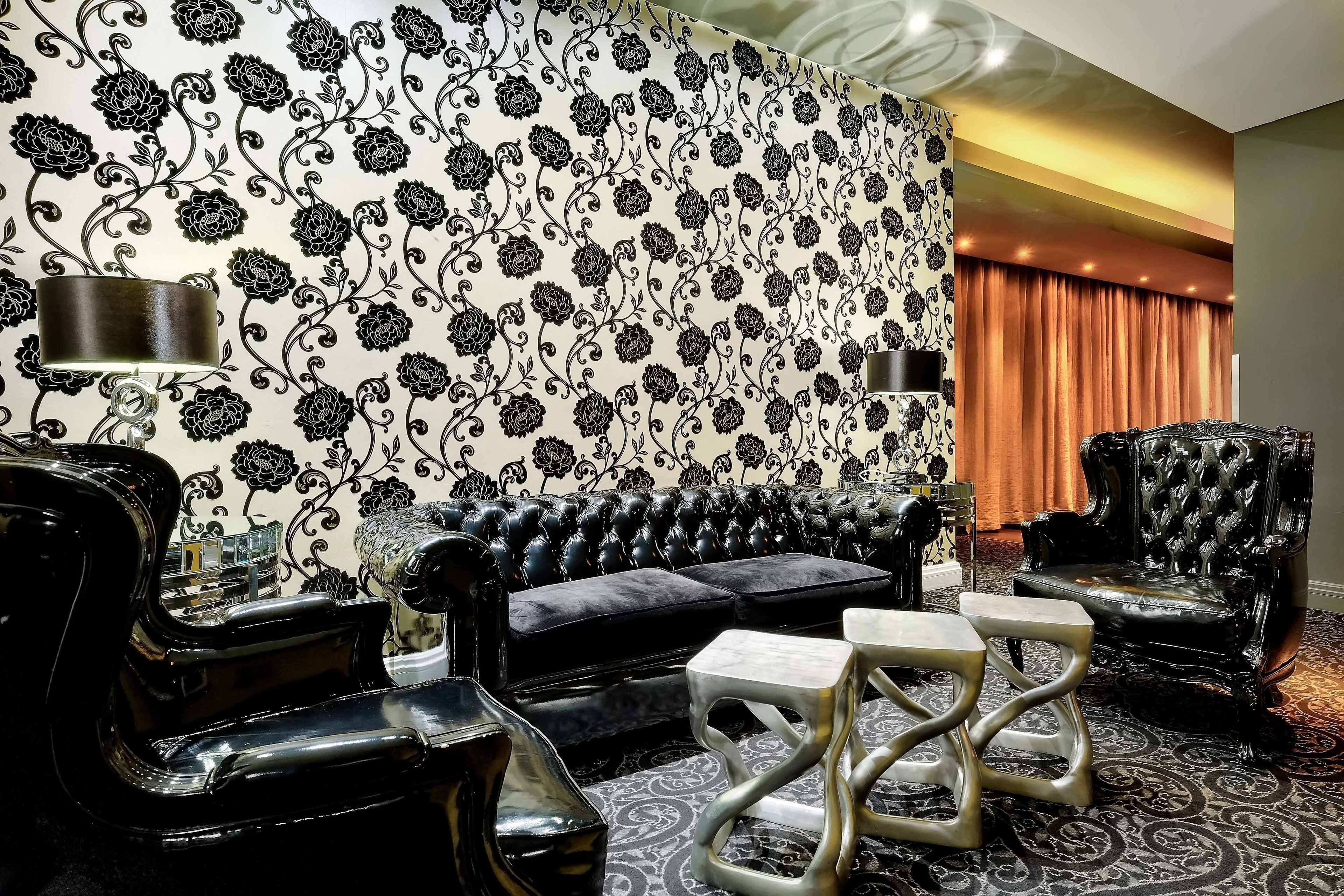 Una habitación lujosa con un sofá de cuero negro, sillones a juego y un papel tapiz estampado.