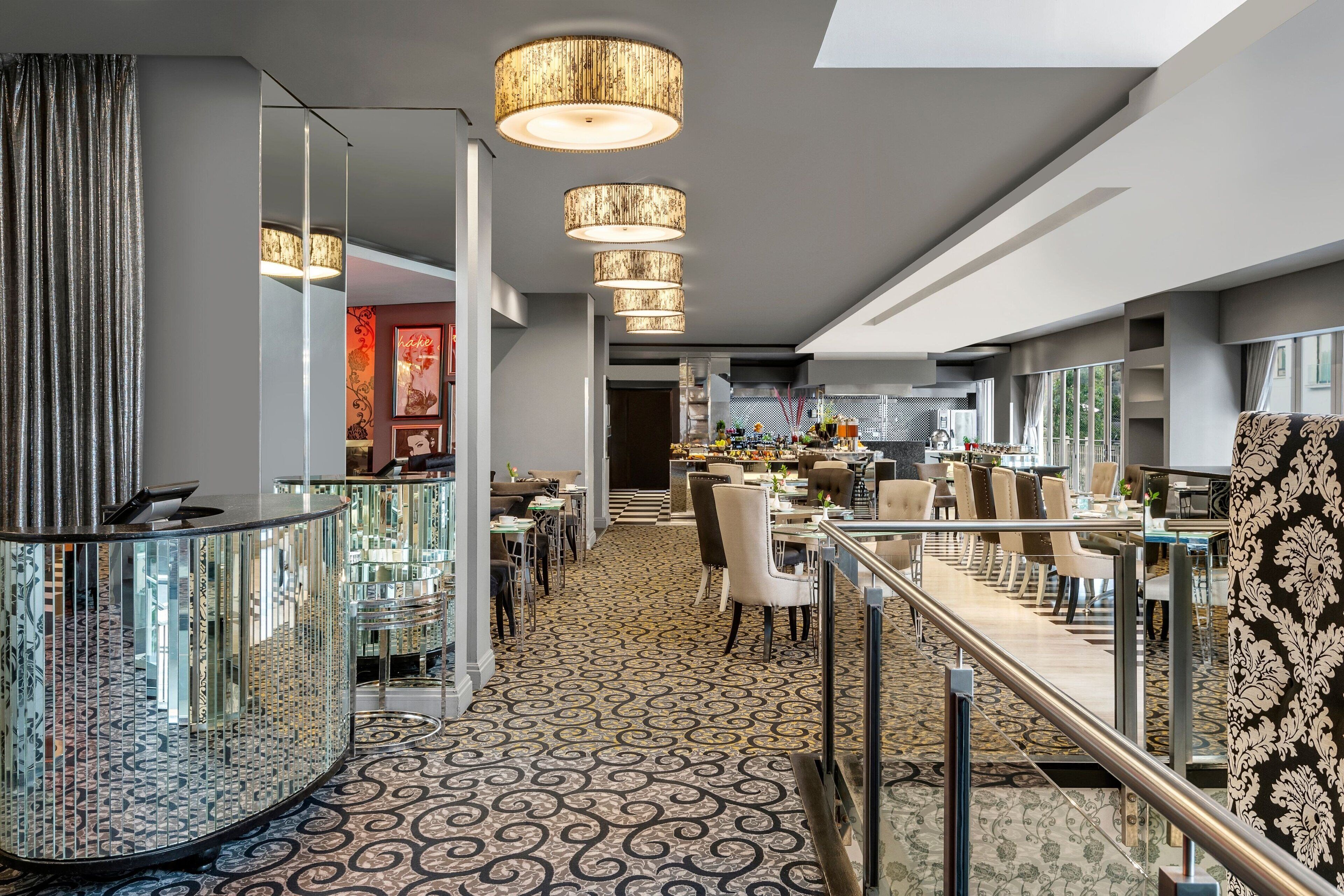 A modern hotel lobby with a central bar area, seating arrangements, and a patterned carpet.