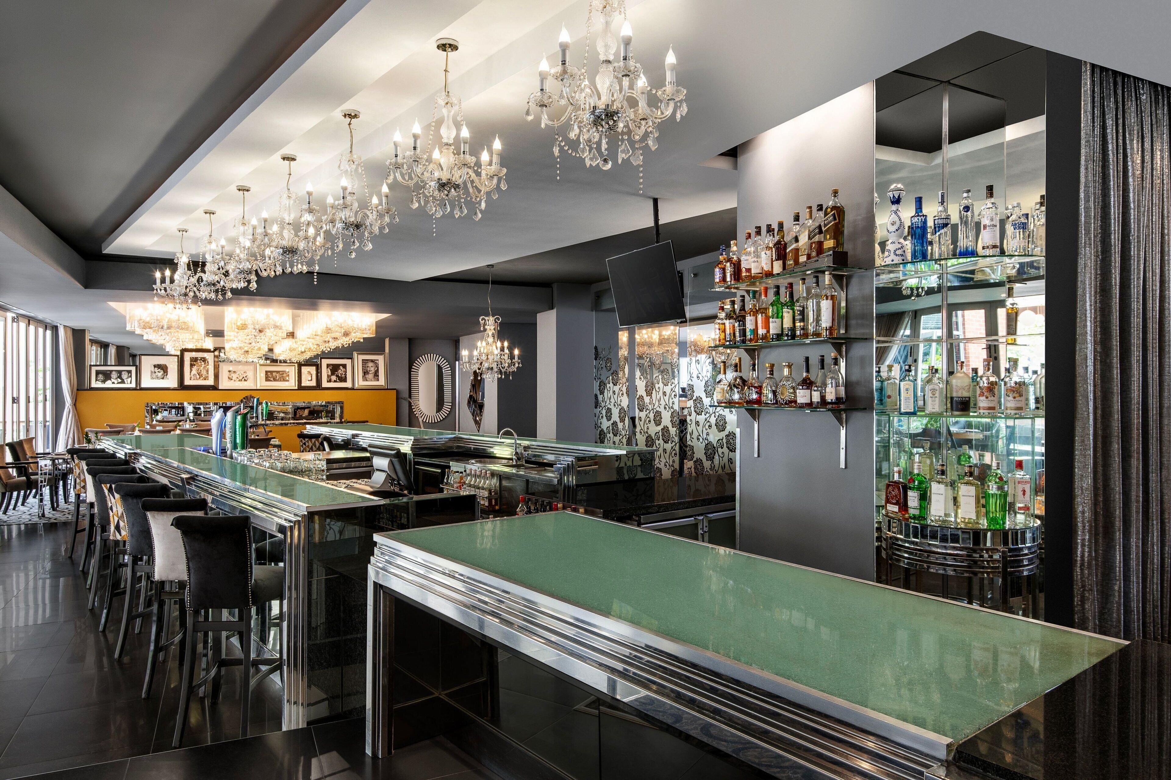 A modern bar area with multiple seating options, a variety of liquor bottles, and elegant chandeliers.