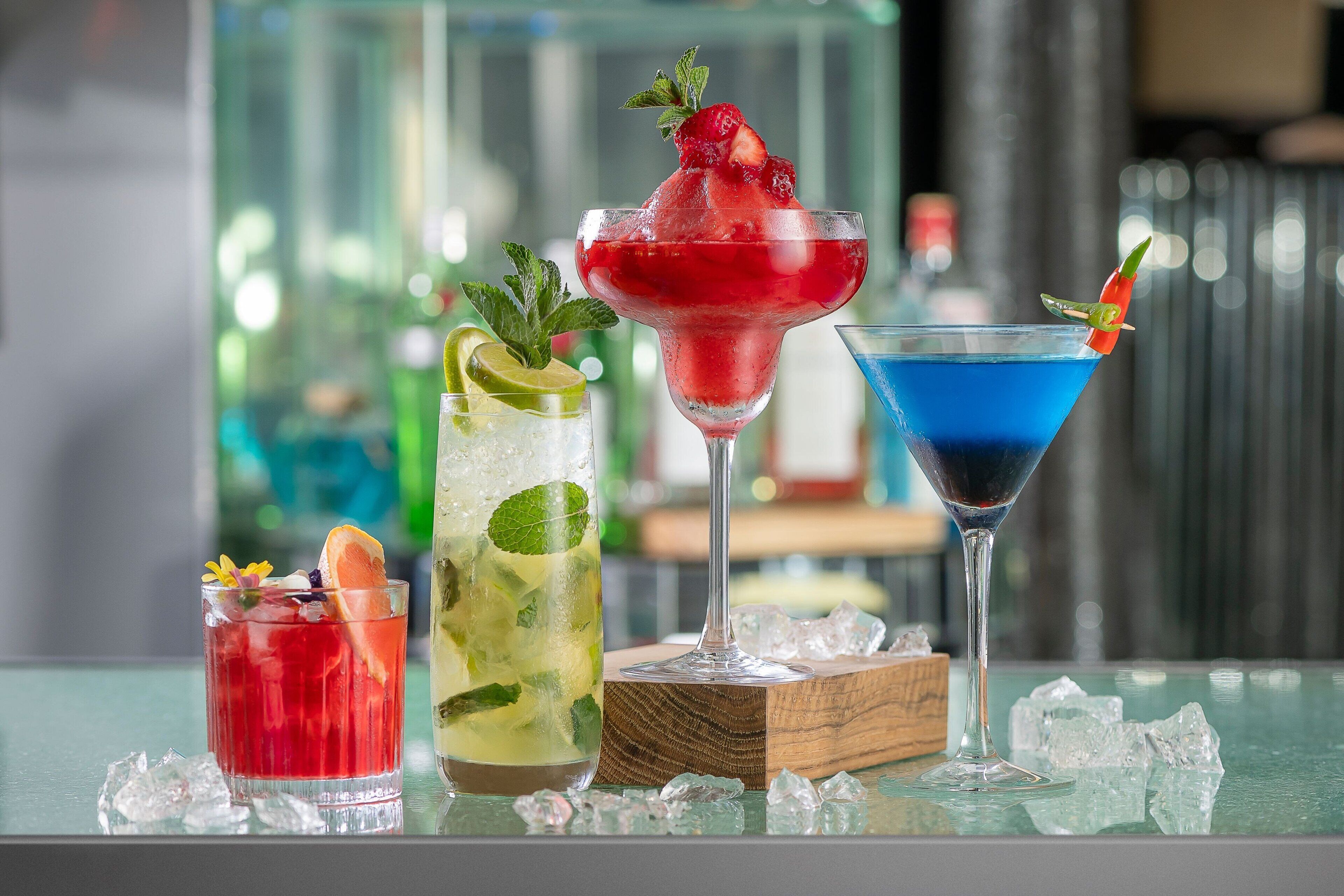 Three cocktails on a bar counter with ice cubes and a blurred background.
