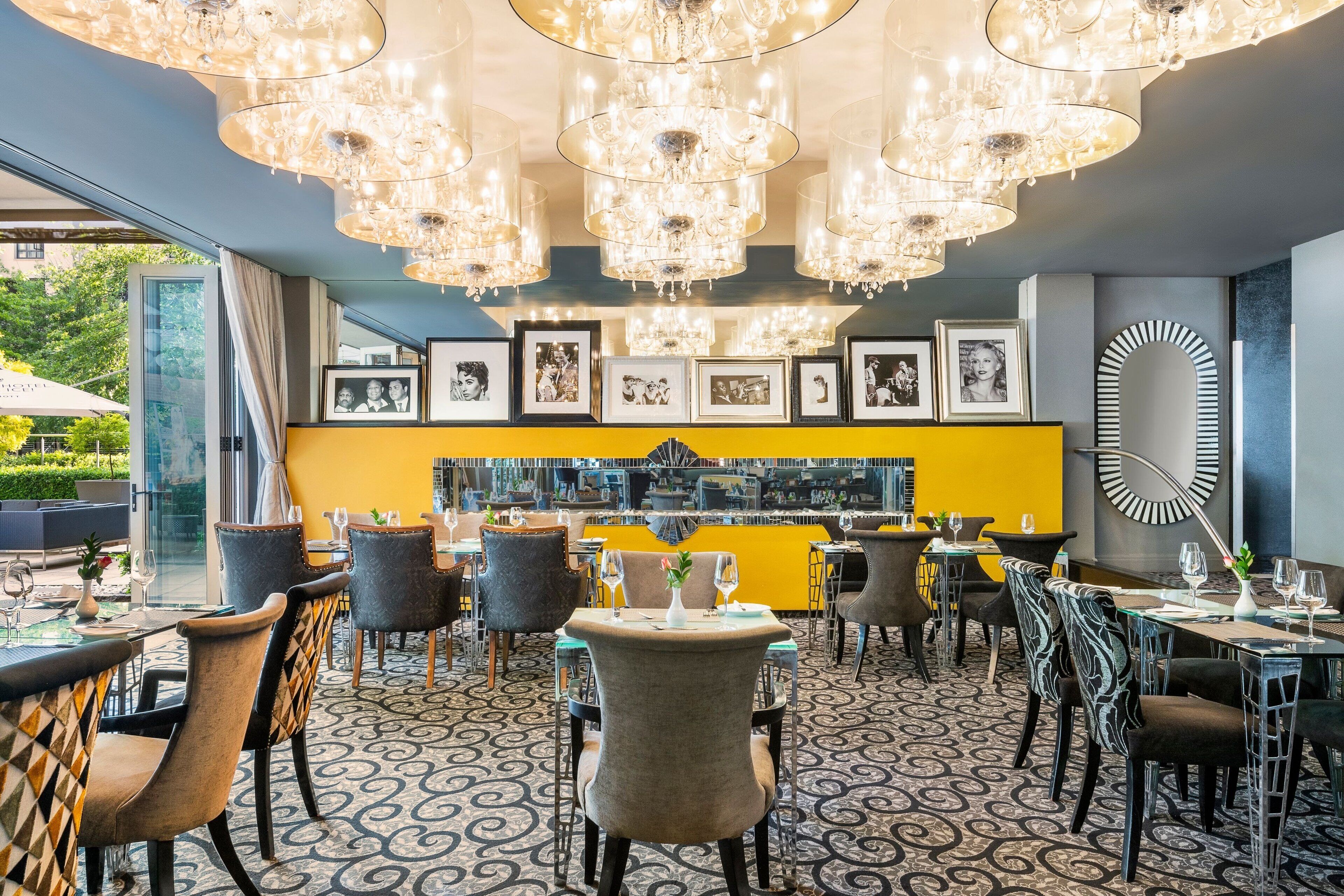 A restaurant with multiple dining areas, chandeliers, framed pictures on the wall, and a yellow accent wall.
