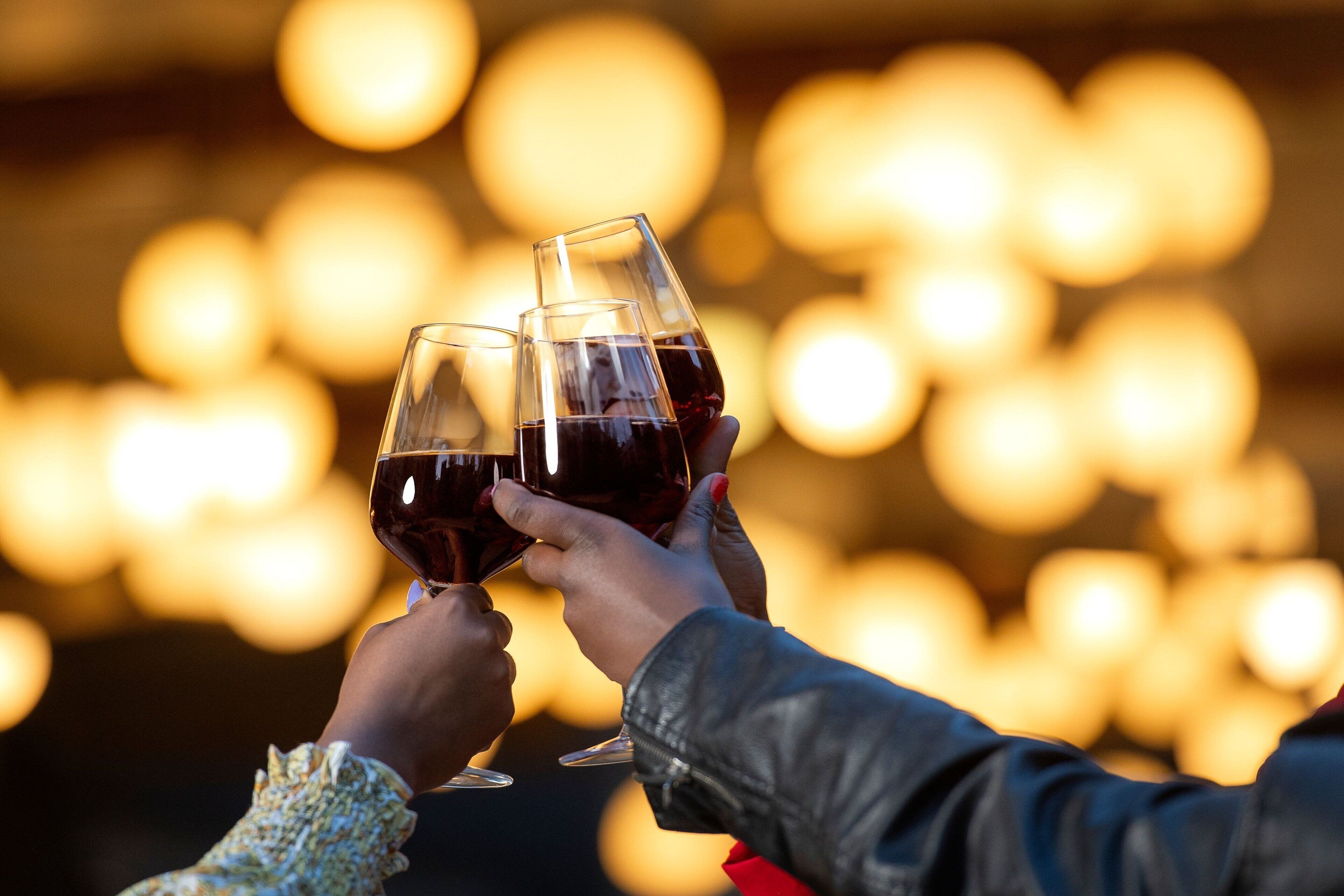 Two people toasting with wine glasses against a blurred background of lights.
