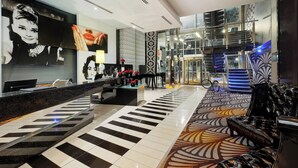 A modern hotel lobby with a reception desk, seating area, patterned carpet, and a staircase.