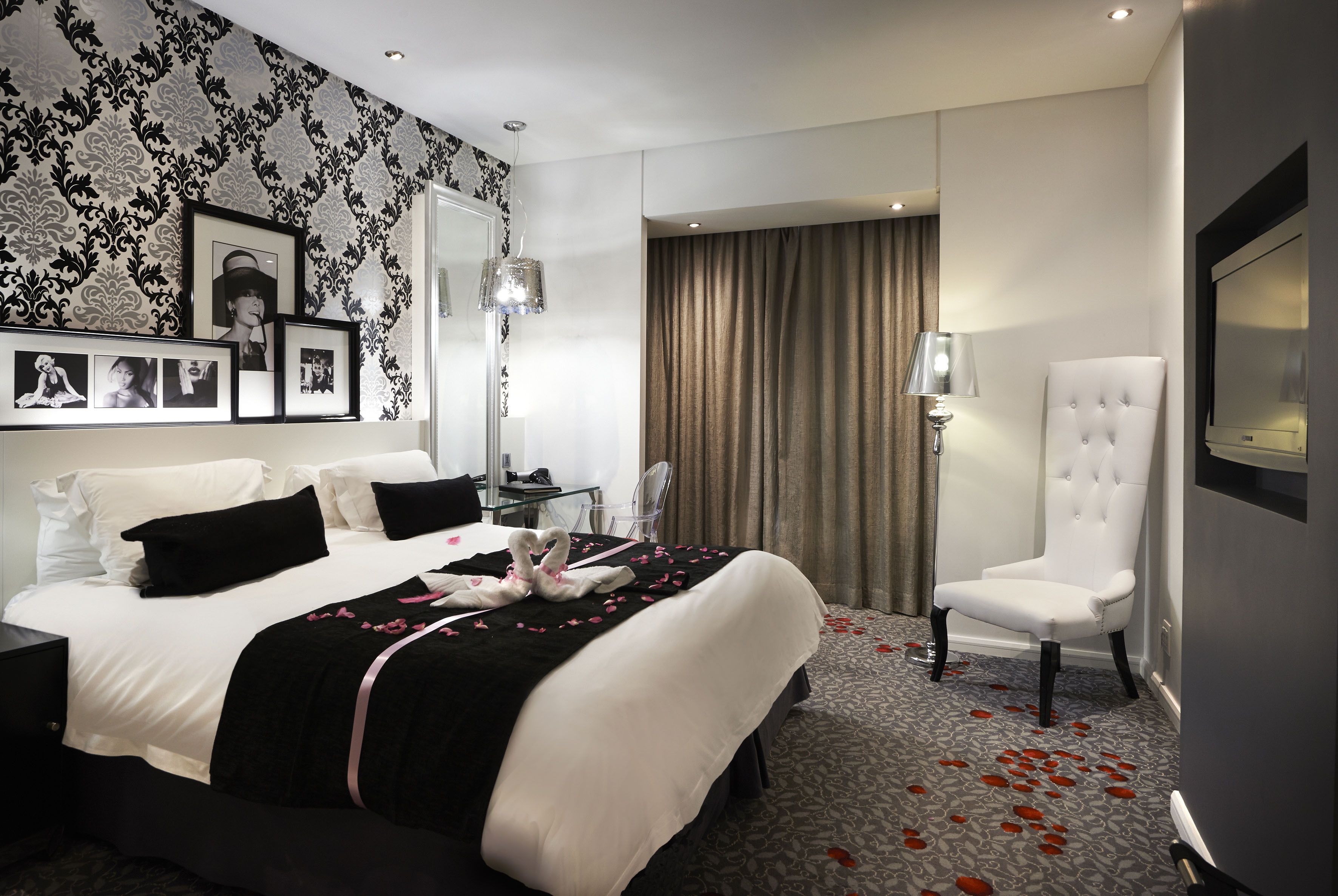 A hotel room with a neatly made bed, a chair, a desk, and a large mirror.