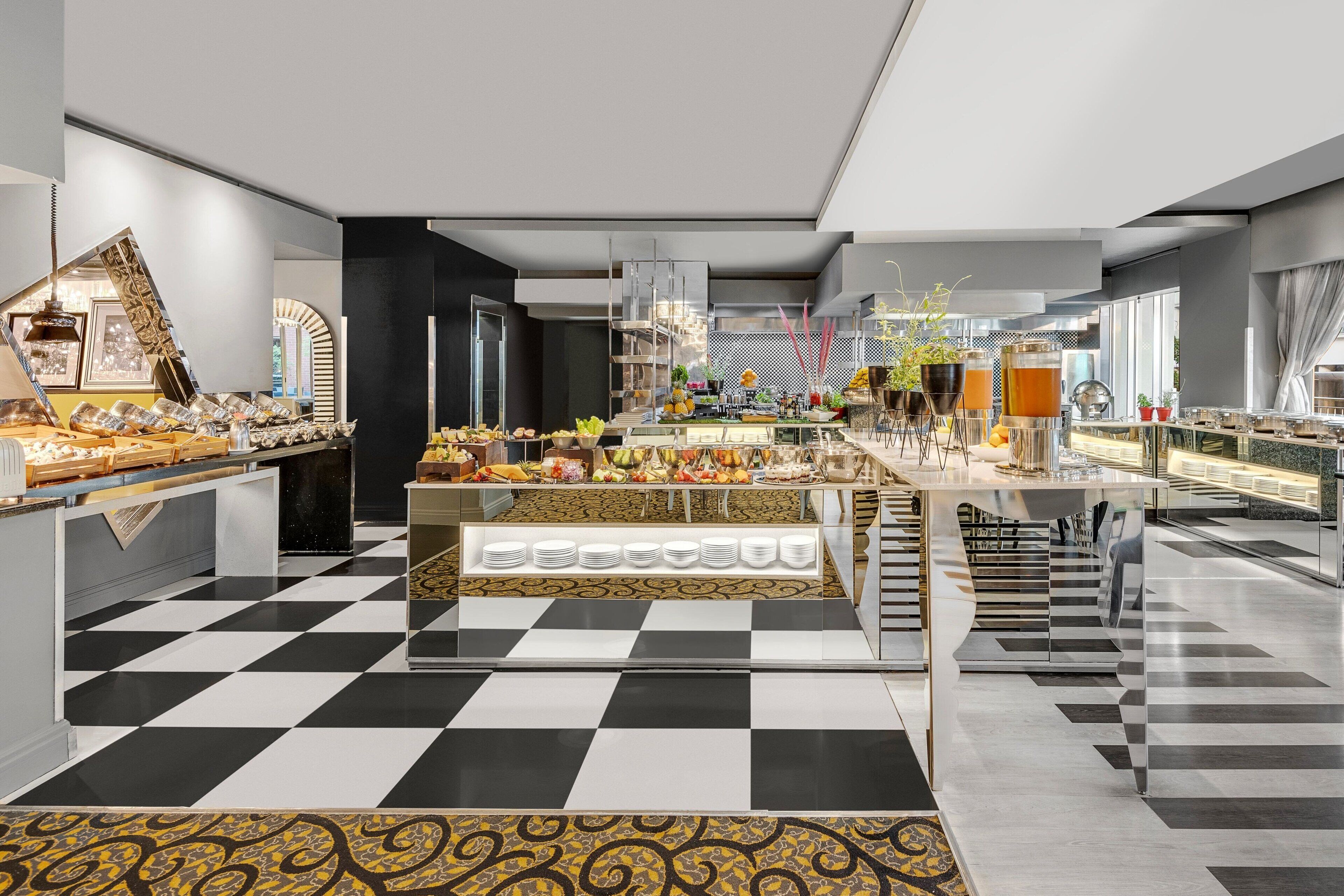 A modern hotel lobby with a checkered floor, a central food display, and a seating area with a view of the outdoors.