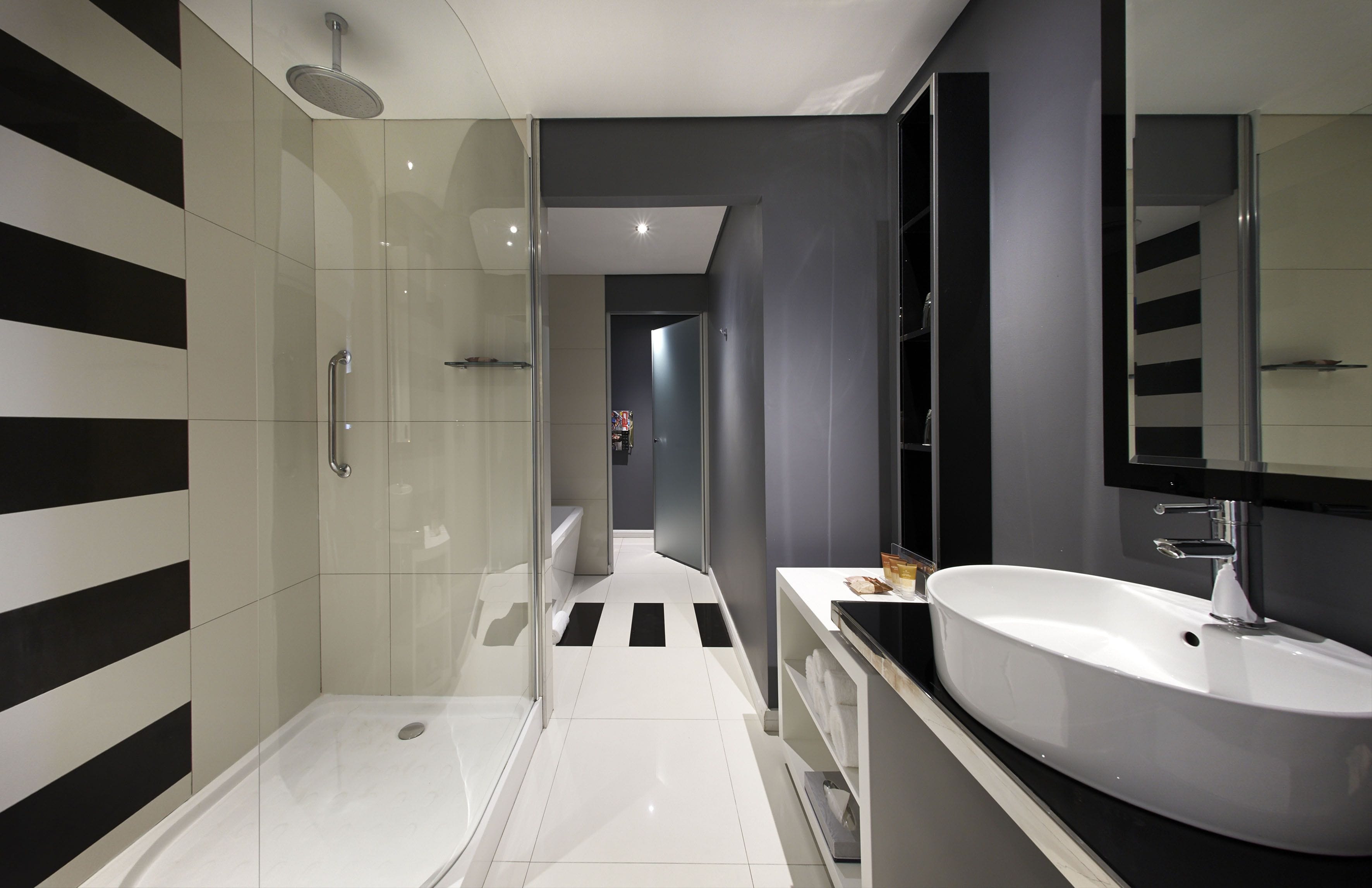 Un baño moderno con ducha envuelta en vidrio, un lavabo blanco y un espejo grande.