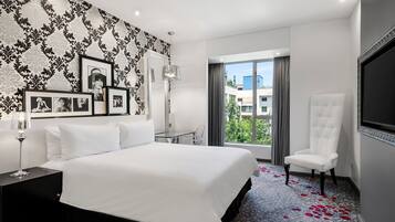 Une chambre d’hôtel moderne avec un grand lit, une table en verre, un fauteuil blanc et un téléviseur fixé au mur.