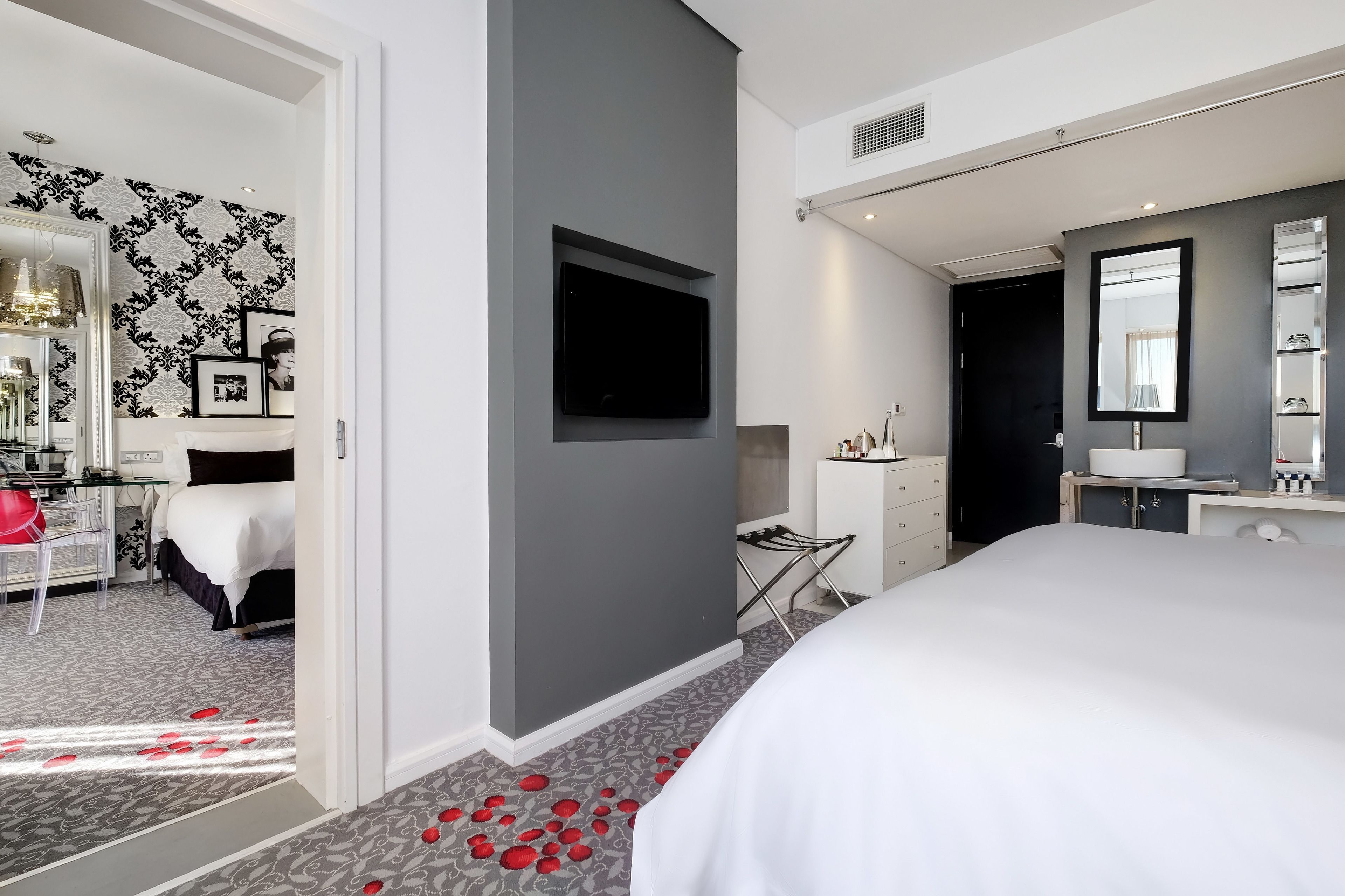 Una habitación de hotel moderna con una cama grande, un televisor de pantalla plana montado en la pared, un tocador con espejo y un escritorio con silla.