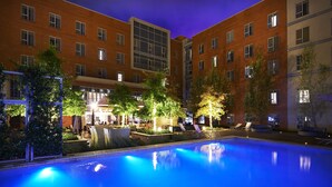 A hotel courtyard with a swimming pool, lounge chairs, and a well-lit outdoor seating area.