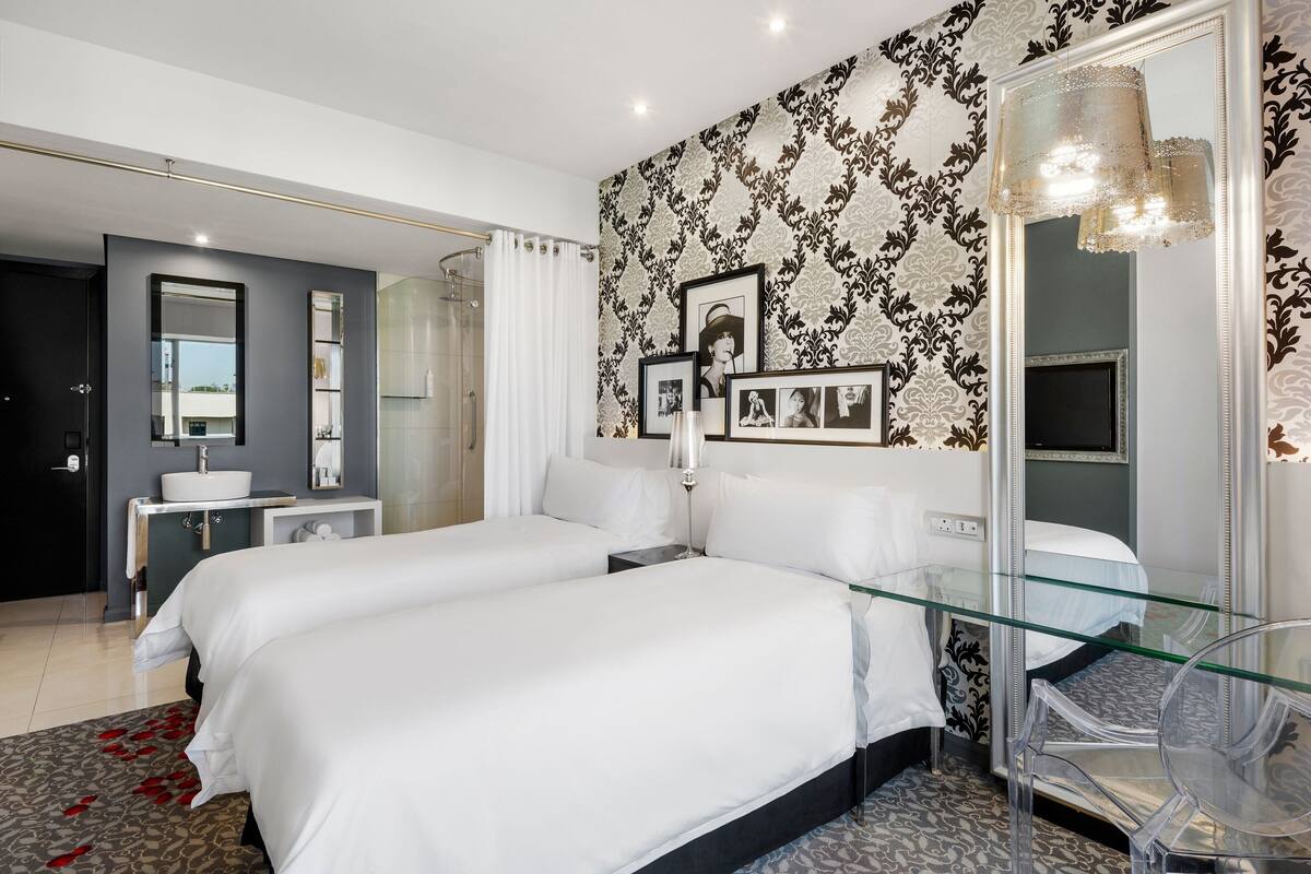 Une chambre d’hôtel moderne avec deux lits, un bureau en verre et un grand miroir.