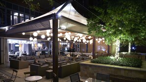 An outdoor seating area with round tables and chairs, a covered patio, and hanging lights.