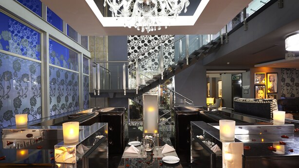 A luxurious hotel lobby with a grand staircase, elegant chandeliers, and a well-lit dining area.