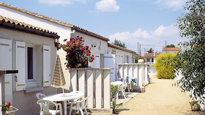 A row of white buildings with shutters, a table with chairs, and a striped umbrella. - Résidence Lagrange Vacances Les Maisons de Saint-Georges (Saint-Georges-de-Didonne)