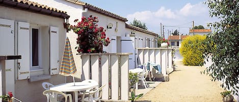 A row of white buildings with shutters, a table with chairs, and a striped umbrella.