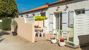 A patio with a table and chairs, a green umbrella, and a white wall with shutters. - Résidence Lagrange Vacances Les Maisons de Saint-Georges (Saint-Georges-de-Didonne)