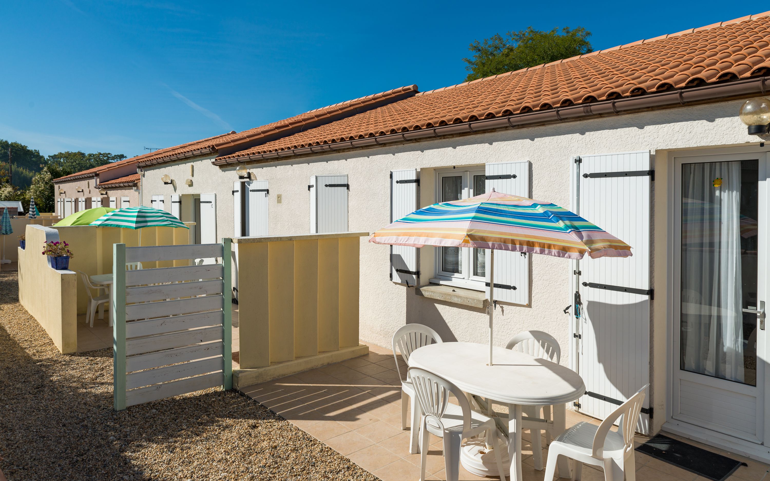 A villa with a tiled roof, white exterior walls, and a patio area with a table and chairs.