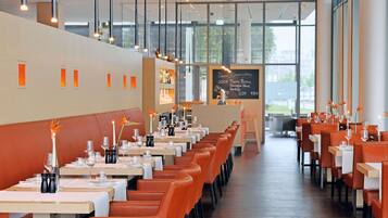 Un restaurant moderne avec de longues tables, des banquettes orange et un menu écrit à la craie.