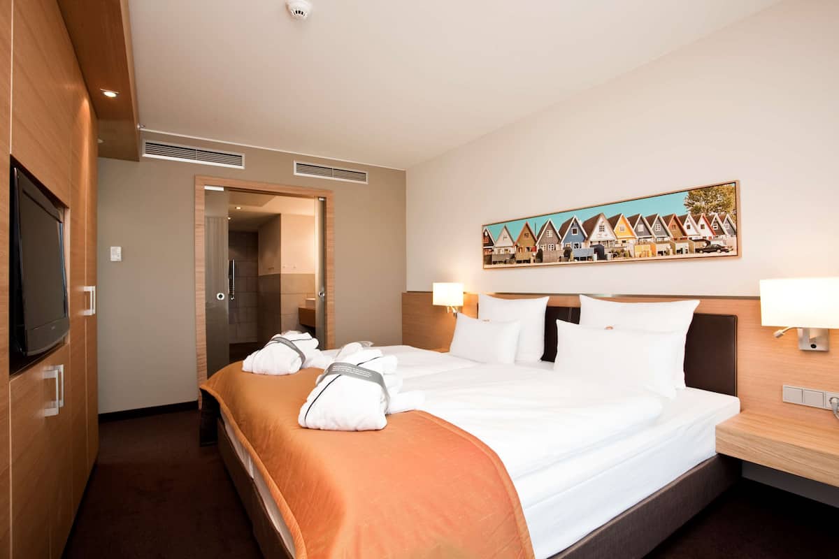 A hotel room with a large bed, a TV, a painting of houses, and a wooden headboard.