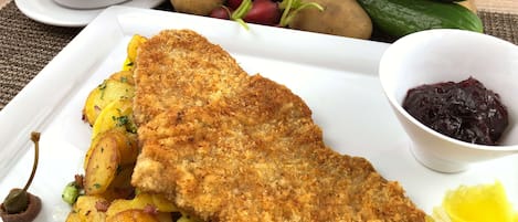 Prato com escalopte empanado, batatas assadas e legumes em conserva.