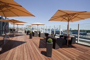 Una terraza en la azotea con suelo de madera, asientos al aire libre y grandes sombrillas.