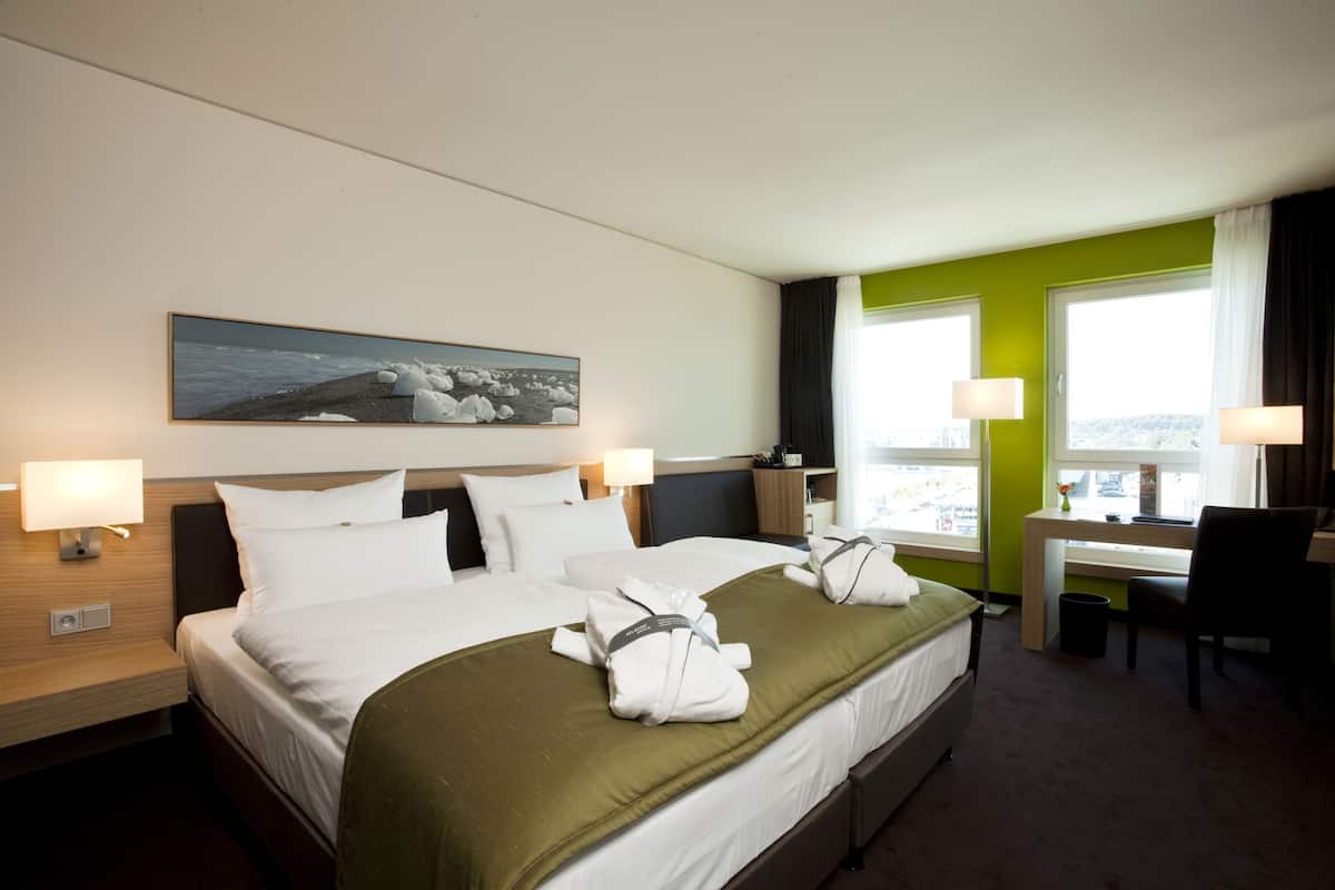 A hotel room with a bed, two bedside tables, a desk, a chair, and a window with curtains.