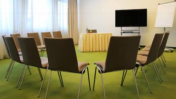 Un salón de conferencias con alfombra verde, sillas marrones, una mesa con mantel amarillo, un televisor de pantalla plana y una pizarra.