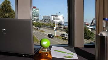 Una computadora portátil sobre un escritorio, con vista a un paisaje urbano a través de amplias ventanas, que incluye un edificio destacado y una masa de agua.