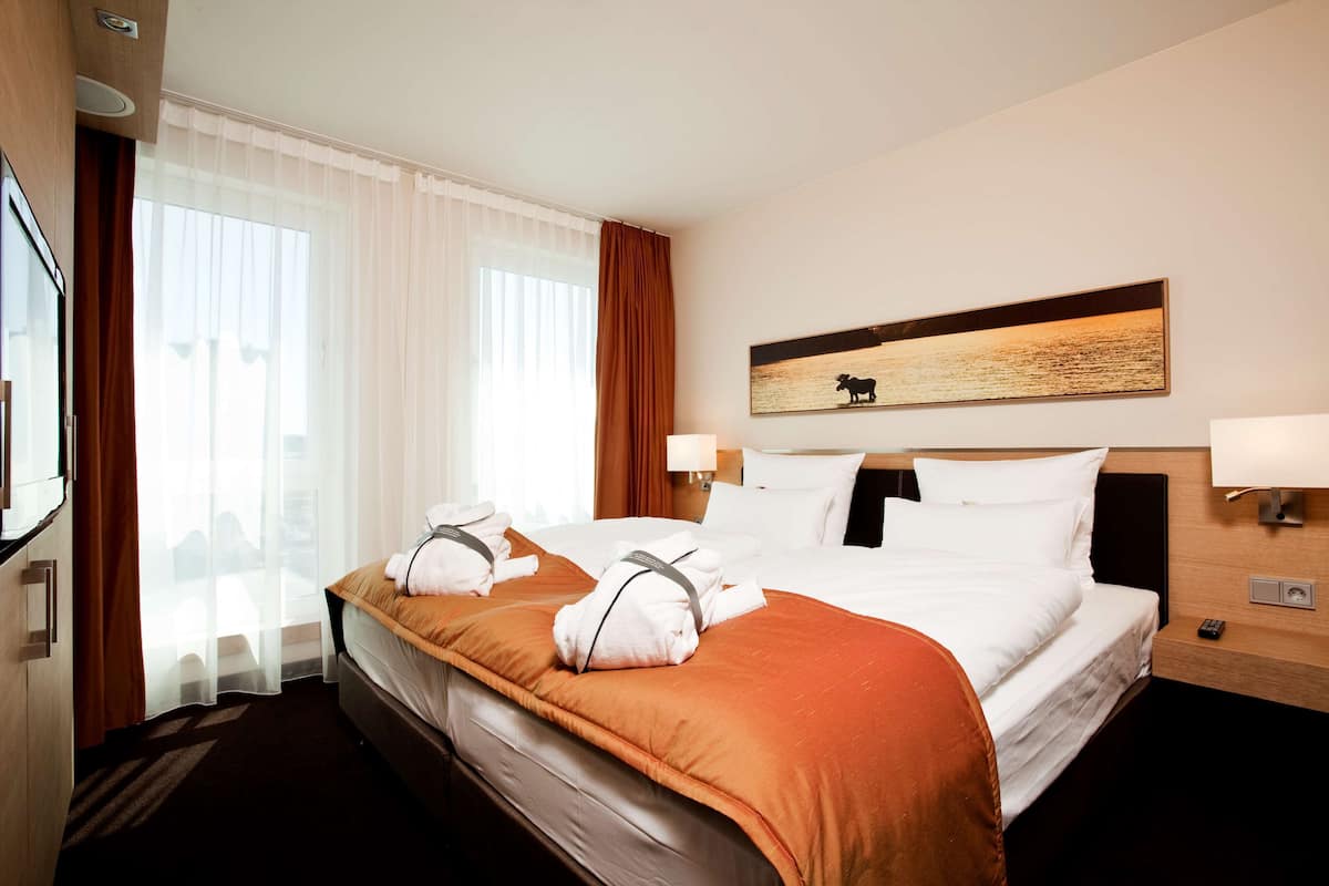 A hotel room with a large bed, two bedside tables, a mounted artwork, and a view of the city through the window.