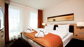 A hotel room with a large bed, two bedside tables, a mounted artwork, and a view of the city through the window.