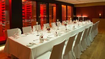 A long dining table set with white tablecloths, chairs, and candles, in a room with red-lit shelving units.