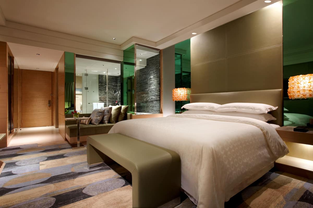 Een moderne hotelkamer met een groot bed, een bankje, een spiegel en een groene wand.