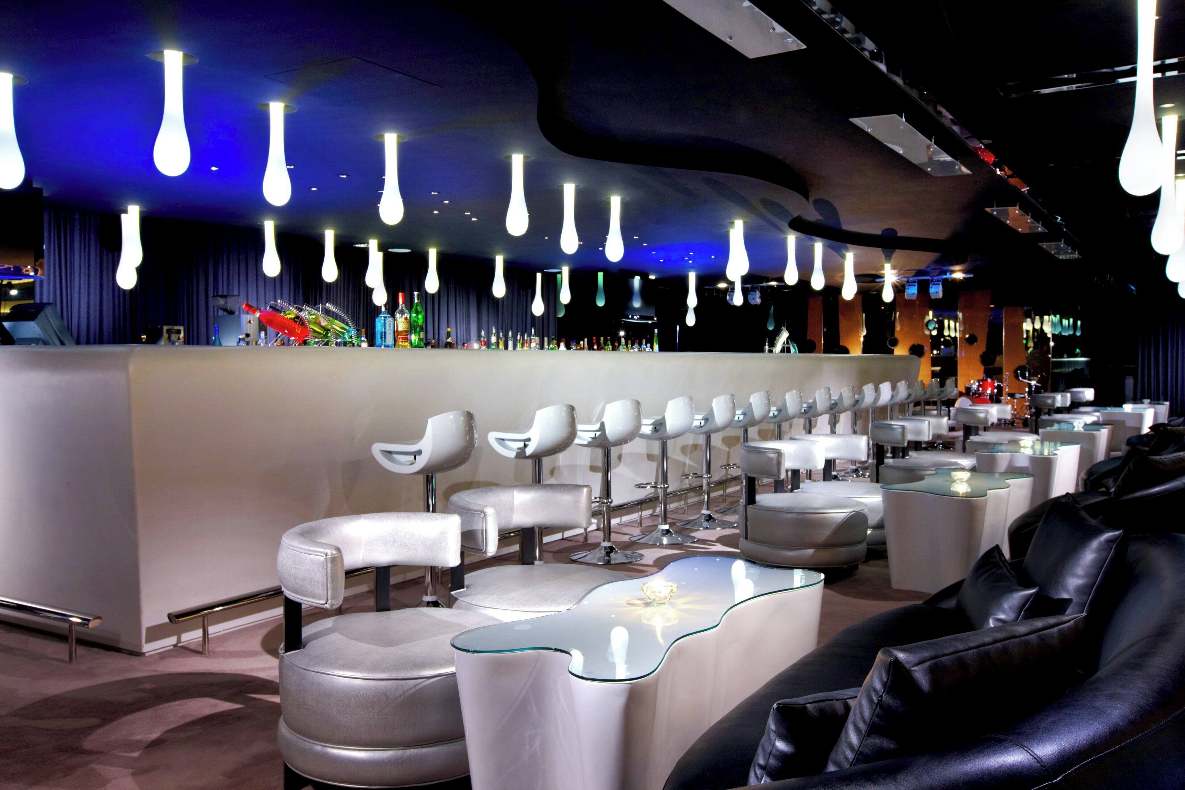 A modern bar area with multiple seating options, including bar stools and cushioned chairs, and a bar counter with a variety of bottles.
