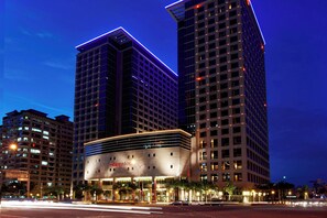Il s’agit d’un hôtel au design moderne, reconnaissable à son grand panneau « Sheraton ». Il compte plusieurs étages, sa façade est structurée en forme de grille et il est entouré d’autres immeubles de grande hauteur.