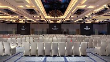 Une salle de conférence d’un hôtel Sheraton, avec des rangées de chaises blanches, une moquette à motifs et un design de plafond moderne.