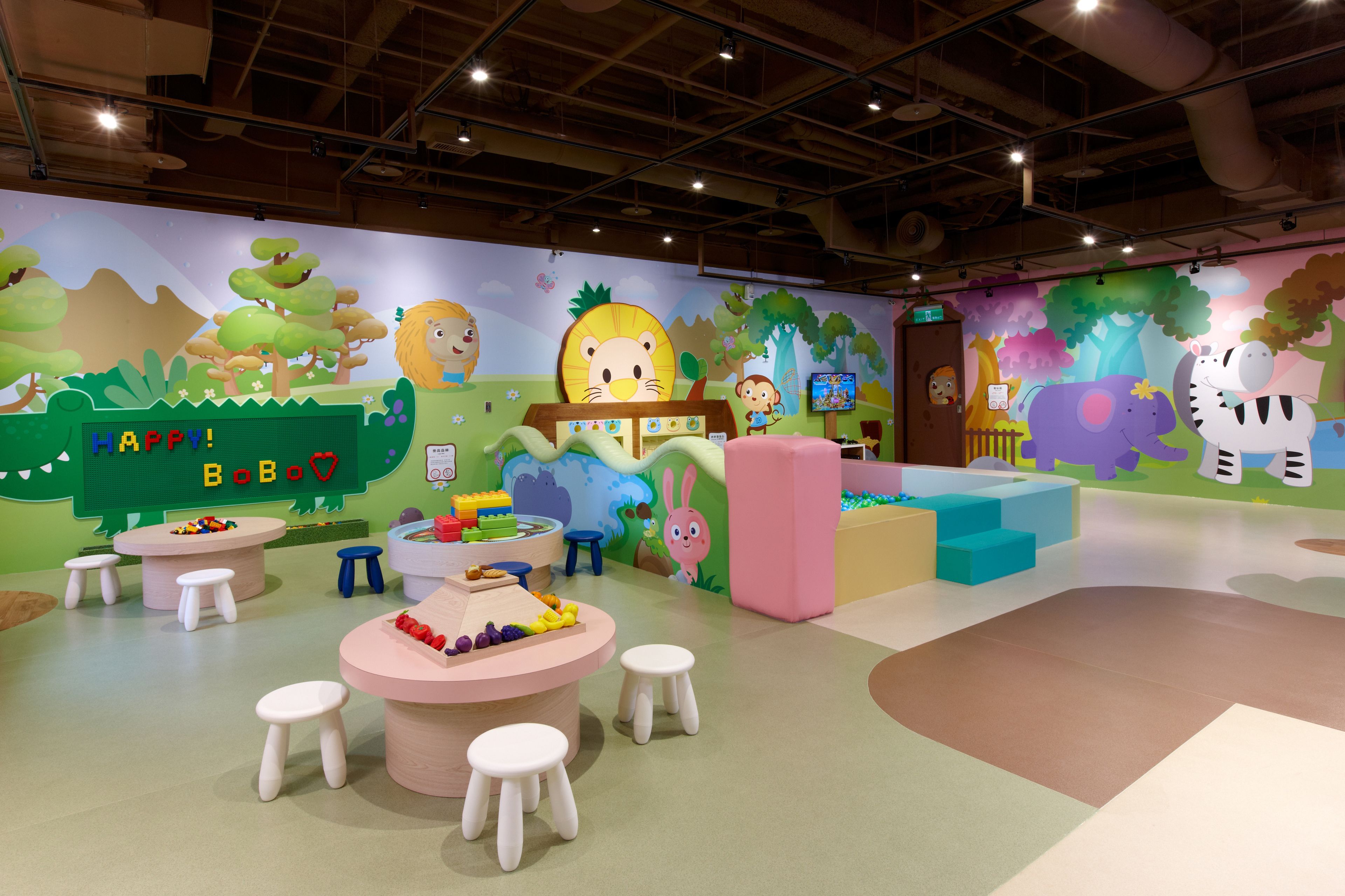 Un'area giochi per bambini con murales colorati, tavoli da gioco e sedute confortevoli.