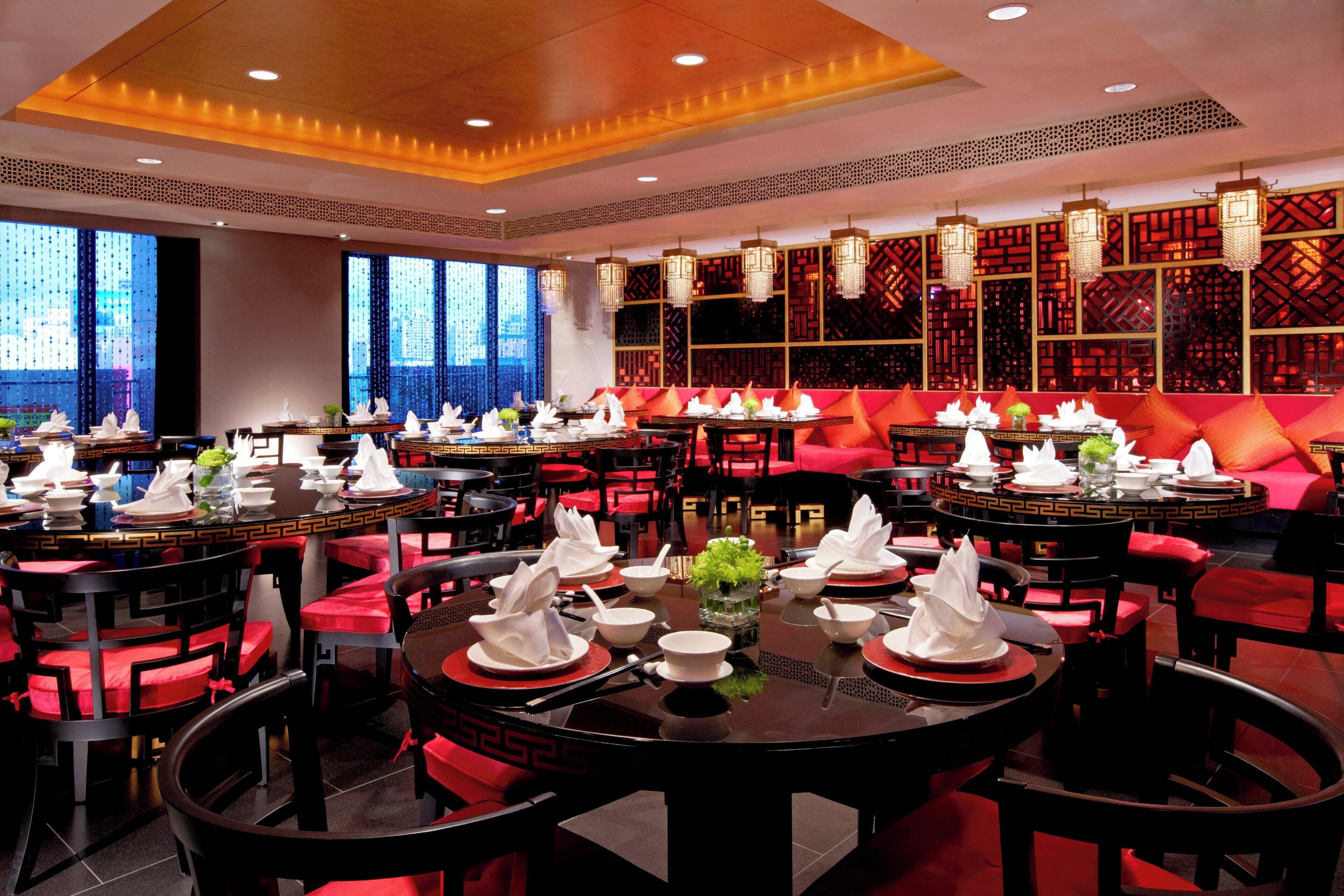 A restaurant with round tables set for dining, red cushioned seating, and traditional decor.
